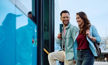 A man and woman await a bus, excited for their visit to Universal Studios Orlando, featuring nearby hotel suites.