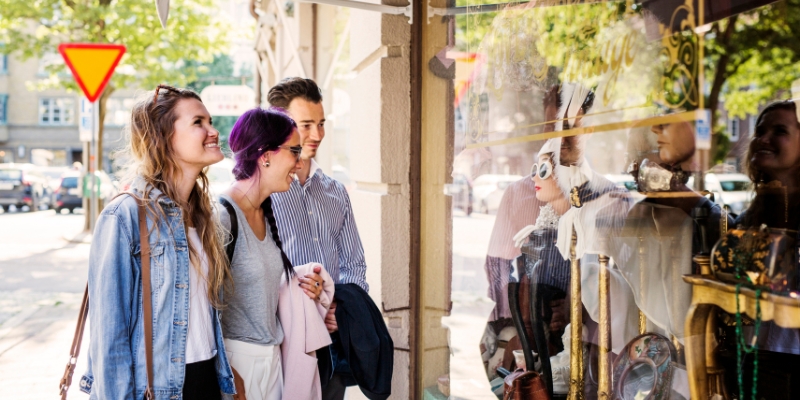 Three individuals observe a shop window filled with boutique merchandise in downtown Orlando.