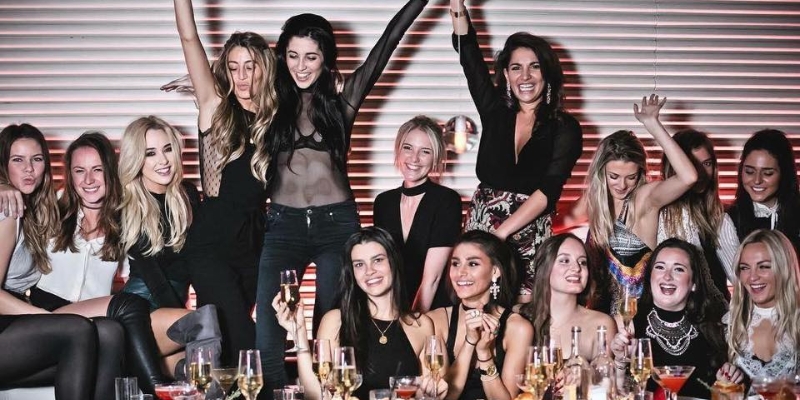 A group of women celebrating at a party, joyfully raising champagne glasses in a vibrant atmosphere.