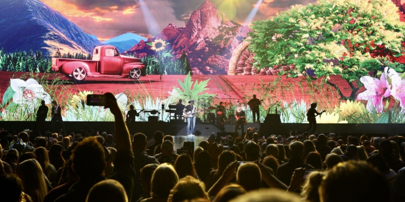 A large crowd enjoys a concert, captivated by the performance displayed on a large screen in KIA Center.