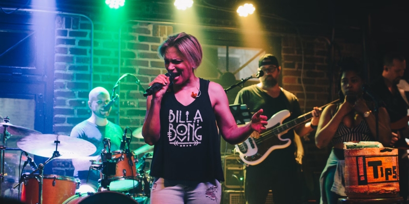 A woman sings energetically on stage, supported by her band, showcasing live music in downtown Orlando for adults.