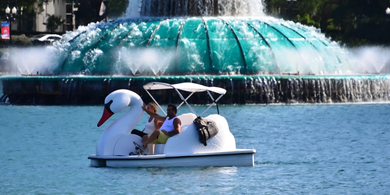 A swan boat floats gracefully in the water beside a fountain, showcasing the beauty of Lake Eola in Downtown Orlando.