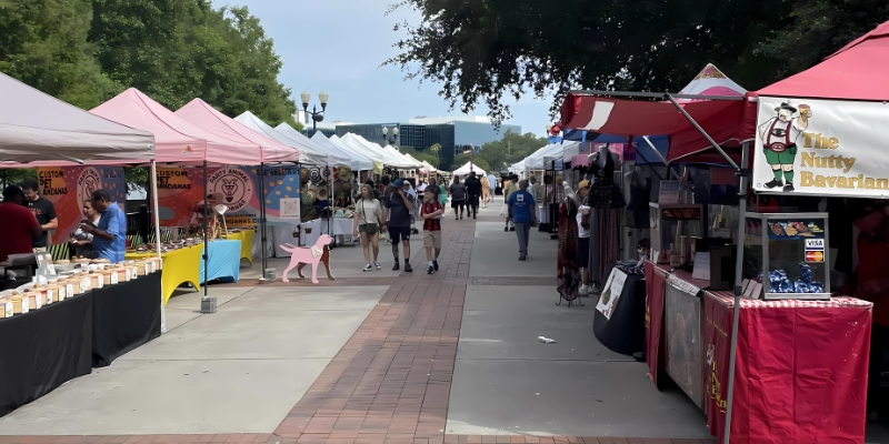 An outdoor market in Thornton Park District, with various tents and booths set up along a lively street, attracting shoppers.