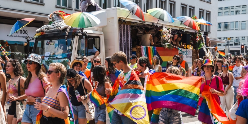 A vibrant crowd walks down the street in downtown Orlando, waving rainbow flags at the Pride Orlando celebration.