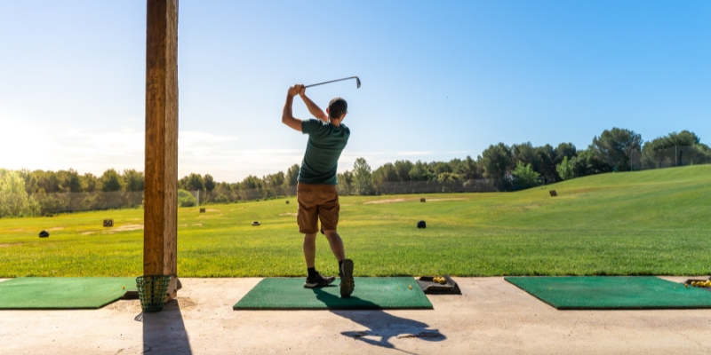 A man in action, hitting a golf ball on a green field, featured in the VIP Golf & Cigar Lounge for an Orlando bachelor party.