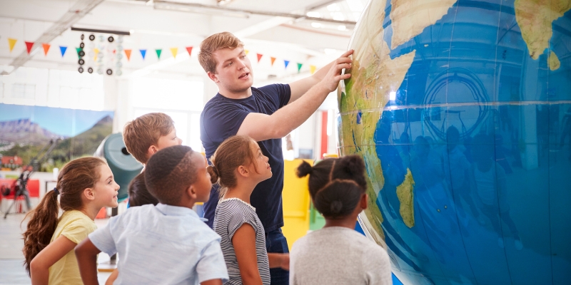 A man gestures towards a globe with children nearby, illustrating Orlando, Florida's rich culture and historical significance.