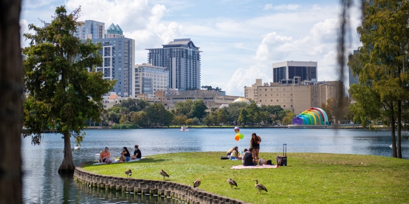A group sits on the grass near Lake Eola, enjoying the view of Orlando's skyline on a sunny August afternoon.