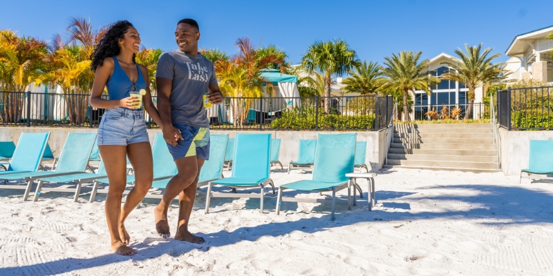A couple enjoys a romantic walk on the beach at a resort, with the sunset illuminating the Promenade at Sunset Walk in Orlando.
