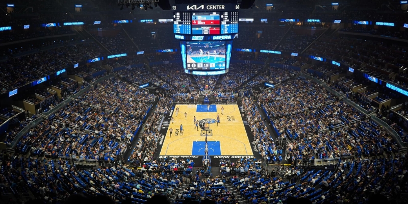 Inside the Kia Center in downtown Orlando, a lively basketball game unfolds with fans enjoying the action in the arena.