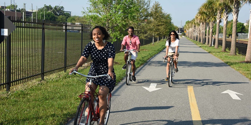 Three people biking on a paved path in downtown Orlando, showcasing the attractions along the Orlando Urban Trail.