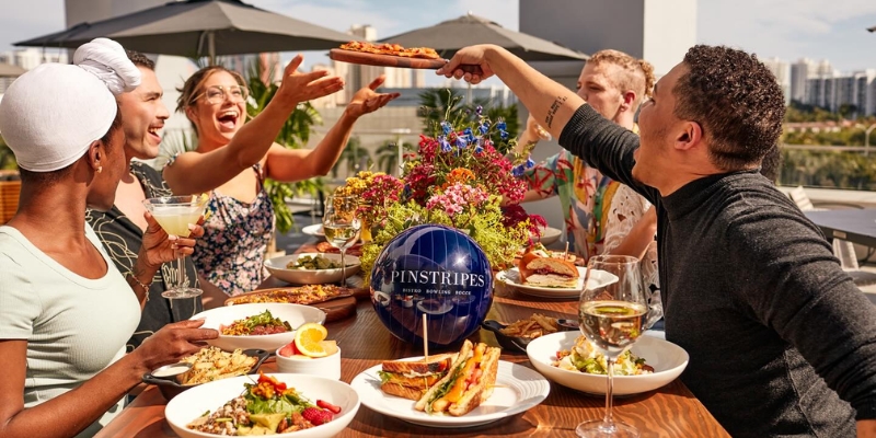 Friends gather at Pinstripes in Orlando for a festive 4th of July meal, enjoying food and laughter in a lively restaurant setting.