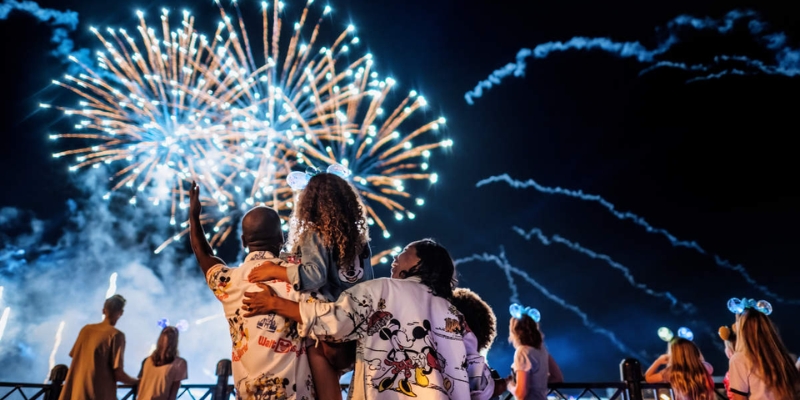 A crowd of individuals admiring a spectacular fireworks show at night, celebrating the Orlando Holidays of Christmas and New Year's.