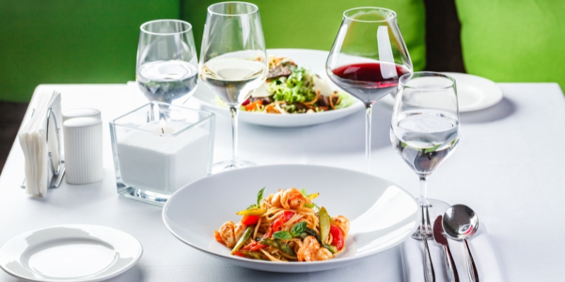 A cozy table with two plates of gourmet food and wine glasses, showcasing a romantic dining experience at Enzo’s on the Lake.