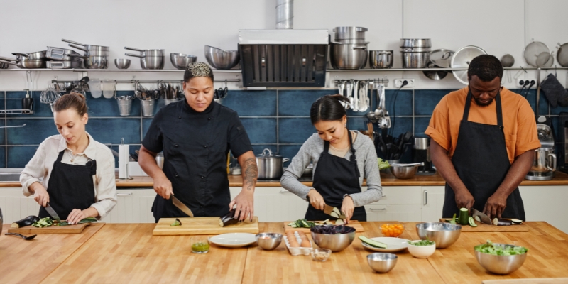 Couples gather in a kitchen, engaged in food preparation during a cooking class at Truffles and Trifles in Orlando.