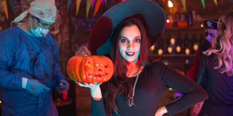 A woman dressed as a witch stands with a pumpkin, embodying the spirit of Halloween in Orlando Holidays.