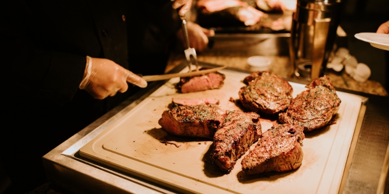 A man skillfully cuts meat on a wooden cutting board at The Capital Grille near the Orlando Convention Center.