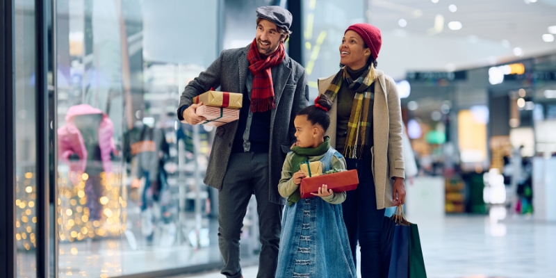 A family strolls through a mall in Downtown Orlando, carrying holiday gifts amidst a festive shopping atmosphere.