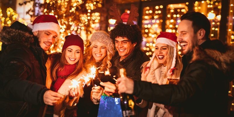 Group of friends joyfully holding sparklers in front of colorful Christmas lights in downtown Orlando.