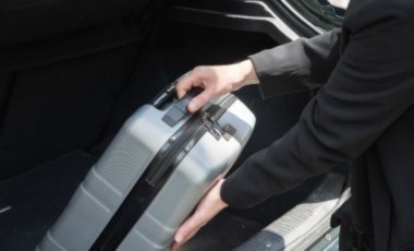 A person in a suit stands by a car trunk, holding a suitcase, near a downtown Orlando hotel by Lake Eola.