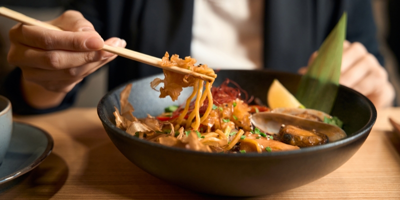 A person enjoying a bowl of pad thai with chopsticks at Mythos Restaurant in Orlando, showcasing a unique dining experience.