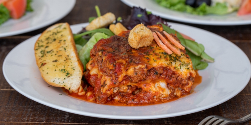 A delicious plate of lasagna, paired with bread and salad, showcasing the culinary offerings at Sleuths Mystery Dinner Shows in Orlando.