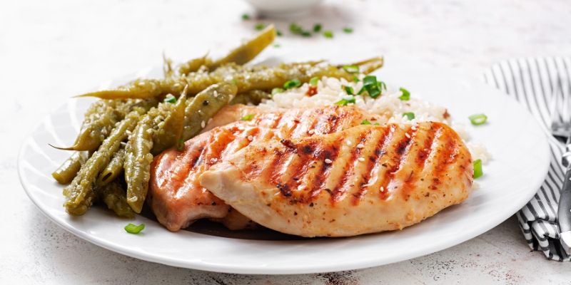 Grilled chicken breast accompanied by green beans and rice on a white plate, showcasing Teatro Martini Orlando's dining offerings.